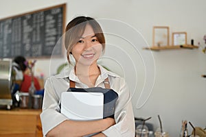 Female barista or coffee shop owner with a digital tablet, standing inside her coffee shop