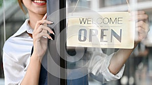 Female barista or coffee shop owner hanging an open welcome sign on the entrance door