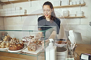 Female barista at showcase with desserts in cafe. Young worker of sweet shop and cafe