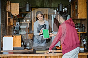 female barista smiling at the customer that pointing on the digital tablet