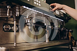 Female barista is tamping espresso fresh ground coffee powder in a metal holder making caffeine