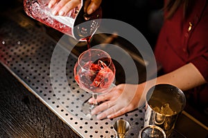 Female barman hands pouring sweet red alcoholic drink into a glass