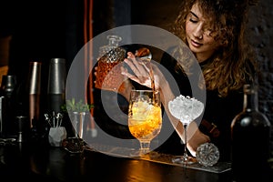 Female bartender carefully pours drink from jigger into glass.