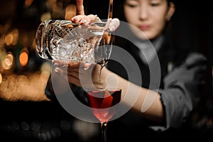 Female bartender pouring alcohol cocktail using strainer