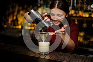 Female bartender pouring out a cocktail from the shaker through the bolter