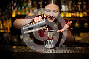 Female bartender pouring out a cocktail from the shaker through the sieve
