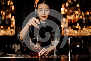 Female bartender stirring alcohol cocktail with bar spoon