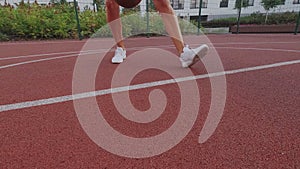 Female basketball player dribbling on city playground. Ball is jumps, bounce. White sneakers and sportswear, tanned skin