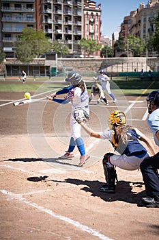 A female batter at the right moment what hits the ball and the catcher behind tries to catch it in a baseball game in the Turia