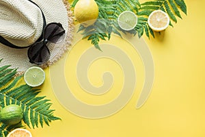 Female beach straw sunhat, sunglasses, citrics on yellow. Top view. Summer travel concept