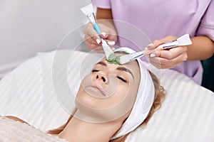 female beautician applies the mask to the face of beautiful woman
