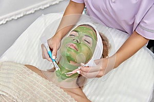 female beautician applies the mask to the face of beautiful woman