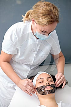 Female beautician applying facial mask treatment to young woman
