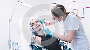 The female beautician doctor making injection in young woman face. The doctor cosmetologist doing facial contouring procedure