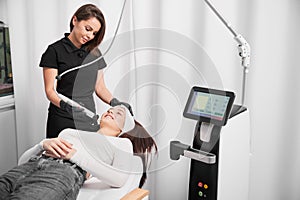 Female beautician performing radiofrequency facial treatment in clinic.