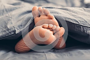 Female beautiful feet under blanket in bed