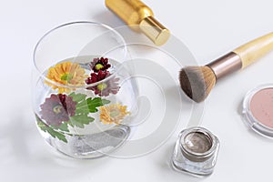 Female beauty accessories flat lay - perfume, Blush, makeup brush, eyeshadows and glass with floating flowers, white background,