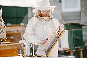 Female beekeper in uniform collecting honey from combs