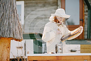 Female beekeper in uniform collecting honey from combs