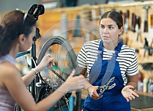 Female bicycle technician explaining repair details to client in workshop