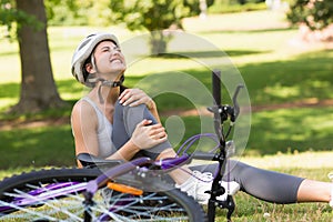 Female bicyclist with hurt leg sitting in park