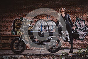 Female biker in black with her motorbike next to graffity wall