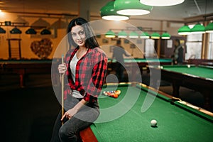 Female billiard player with cue poses at the table