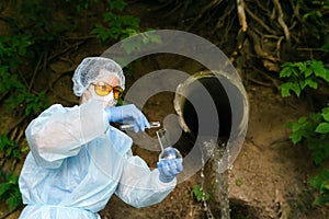 Female biochemist or infectious disease specialist conducts a chemical test of water against the background of a sewer with