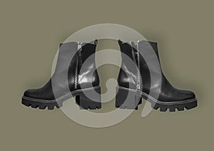 Female black leather boots on thick soles and high heels isolated on brown background. Tractor-soled boots