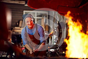 Female Blacksmith Heating Metalwork In Flames Of Forge