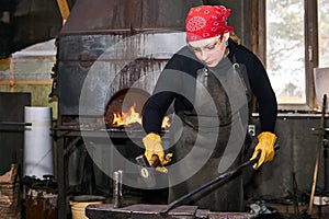 Female blacksmith metal artist forge a hot metal billet on the anvil