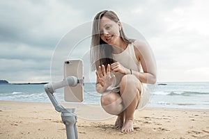 A female blogger shoots herself in a video blog by the sea in a mobile phone. A young woman waves and smiles in greeting