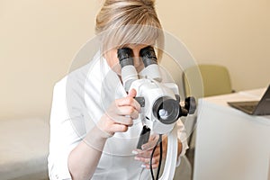 Female blond doctor gynecologist looks through a colposcope. Examination by a gynecologist. Female health concept