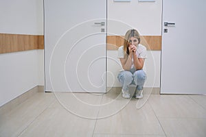 Female blonde woman in jeans is squatting in hospital corridor