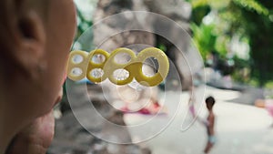 Female blows soap bubbles in the garden, children run in the background, slow motion