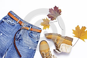 Female blue jeans, boots and autumn leaves on green background top view flat lay. Fashion Lady Clothes Set Trendy Cozy Knit Jumper