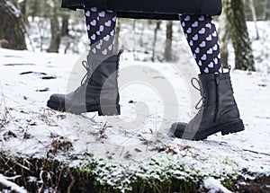 Female boots on snowy path, side view. Legs walking or strolling in winter forest in funny cute tights with hearts print for 14