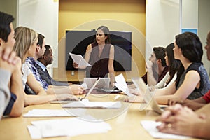 Female Boss Addressing Meeting Around Boardroom Table