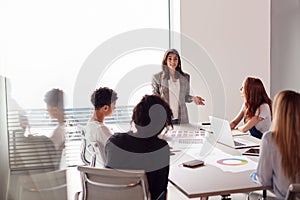 Female Boss Gives Presentation To Team Of Young Businesswomen Meeting Around Table In Modern Office