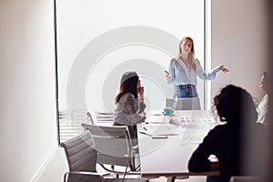 Female Boss Gives Presentation To Team Of Young Businesswomen Meeting Around Table In Modern Office