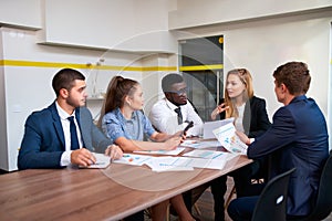 Female boss leads global business brief with multicultural team in modern office, discussing graphs. Diverse group of