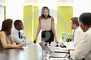 Female boss stands addressing team at informal work meeting