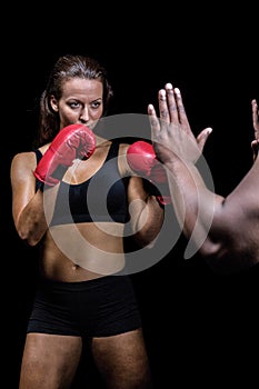 Female boxer with fighting stance against trainer hand