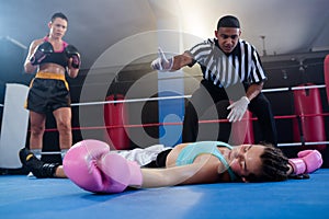 Female boxer looking while referee counting by athlete