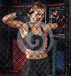 Female boxer posing inside a boxing cage.
