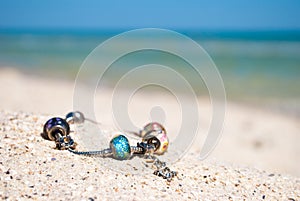 Female bracelet decoration lies on the sand on a background of blue sea and blue sky