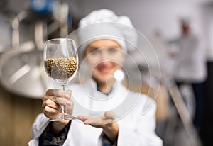 Female brewer demonstrating high quality malted barley grain in glass