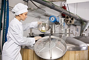 Female brewmaster pouring hop pellets from bowl into fermenter