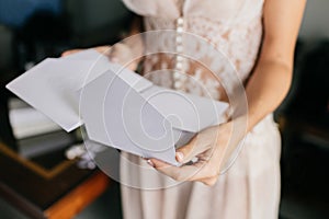 Female bride in white dress, holds white letter or envelope, prepares for invitation, prepares for wedding ceremony. Marriage