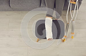 Female broken injured leg relaxing on stool in cast and metal crutches